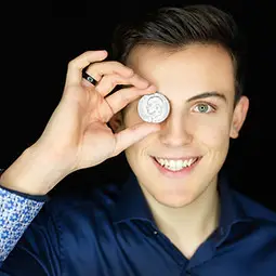 Moritz Neumeister hält eine Münze vor seinem Auge